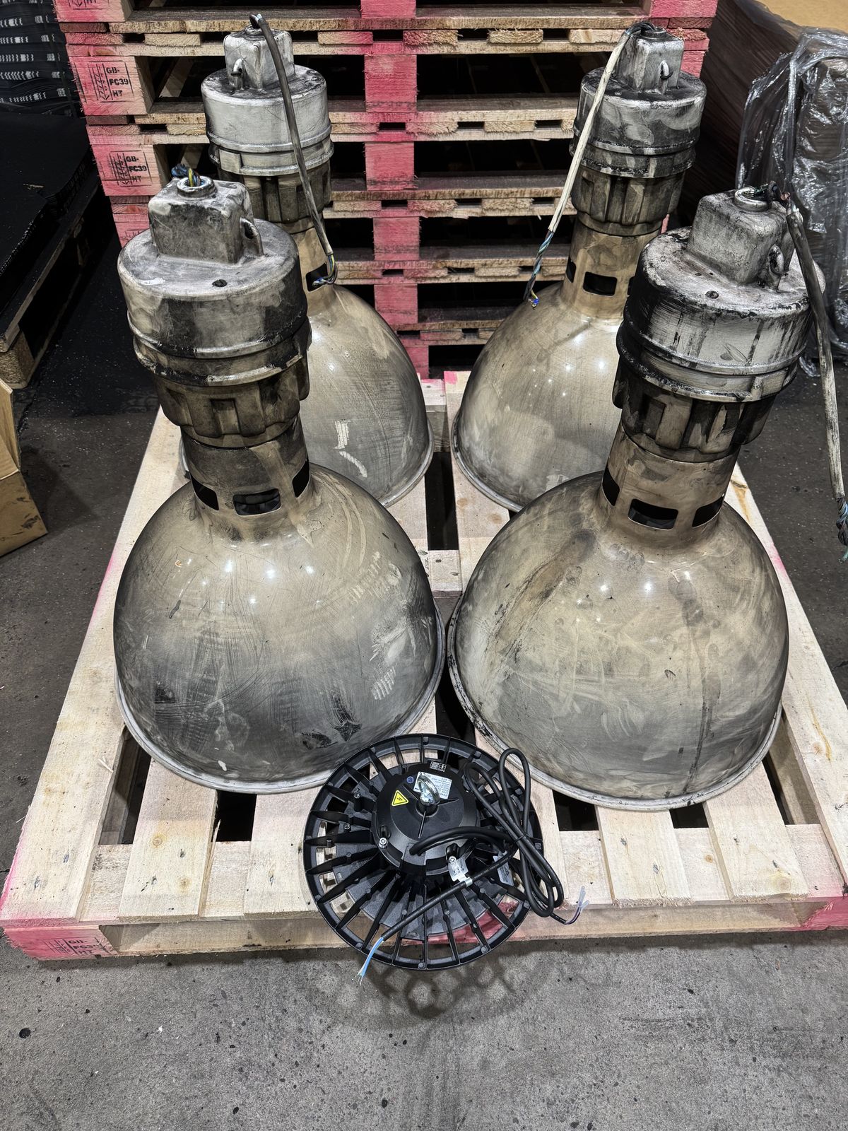 Four old 750W high-pressure sodium high bay fittings on a pallet next to one new compact 200W LED high bay, showing the dramatic size difference between old and new technology
